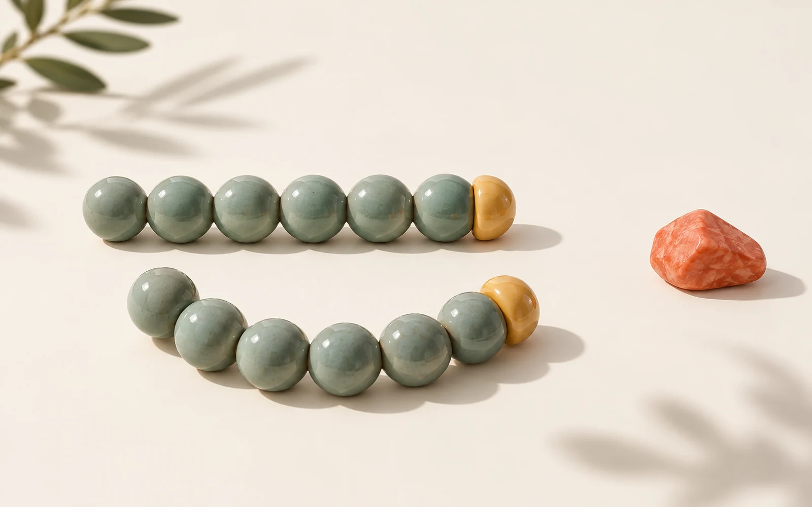 Deux chaînes de perles jade à embout ambré, l’une presque droite et l’autre incurvée, sur fond crème.