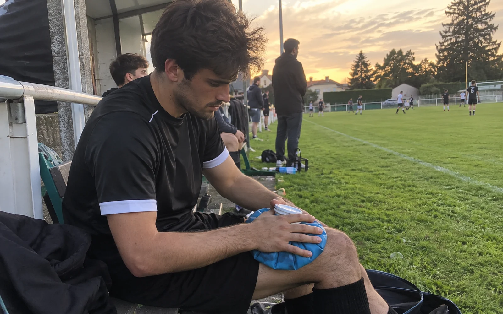 Jeune footballeur amateur assis au bord du terrain avec une poche de glace sur le genou.