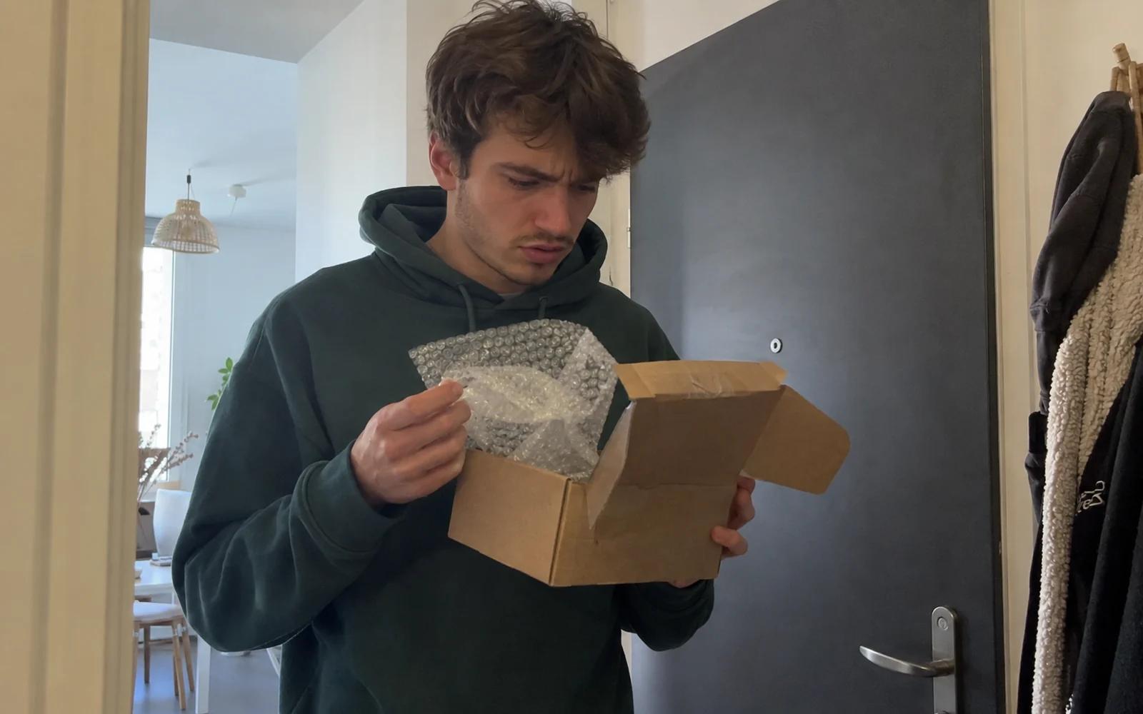 Jeune homme inspectant d’un air méfiant un colis en carton qu’il vient d’ouvrir.