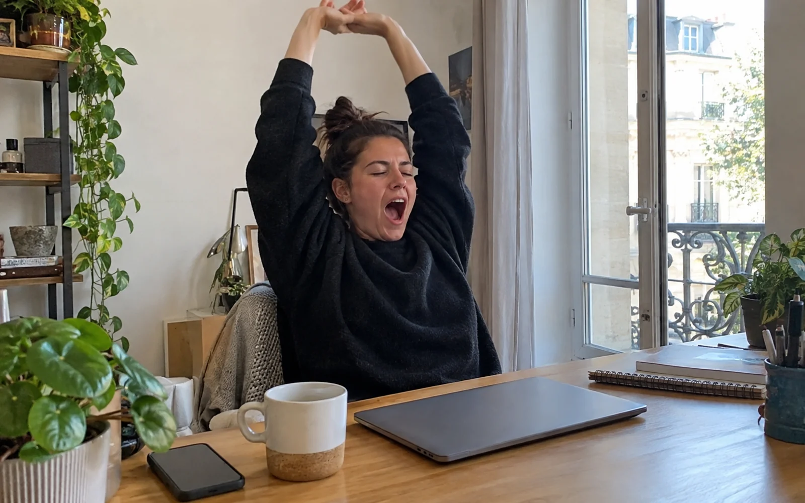 Jeune femme qui s’étire en bâillant à son bureau en milieu d’après-midi.