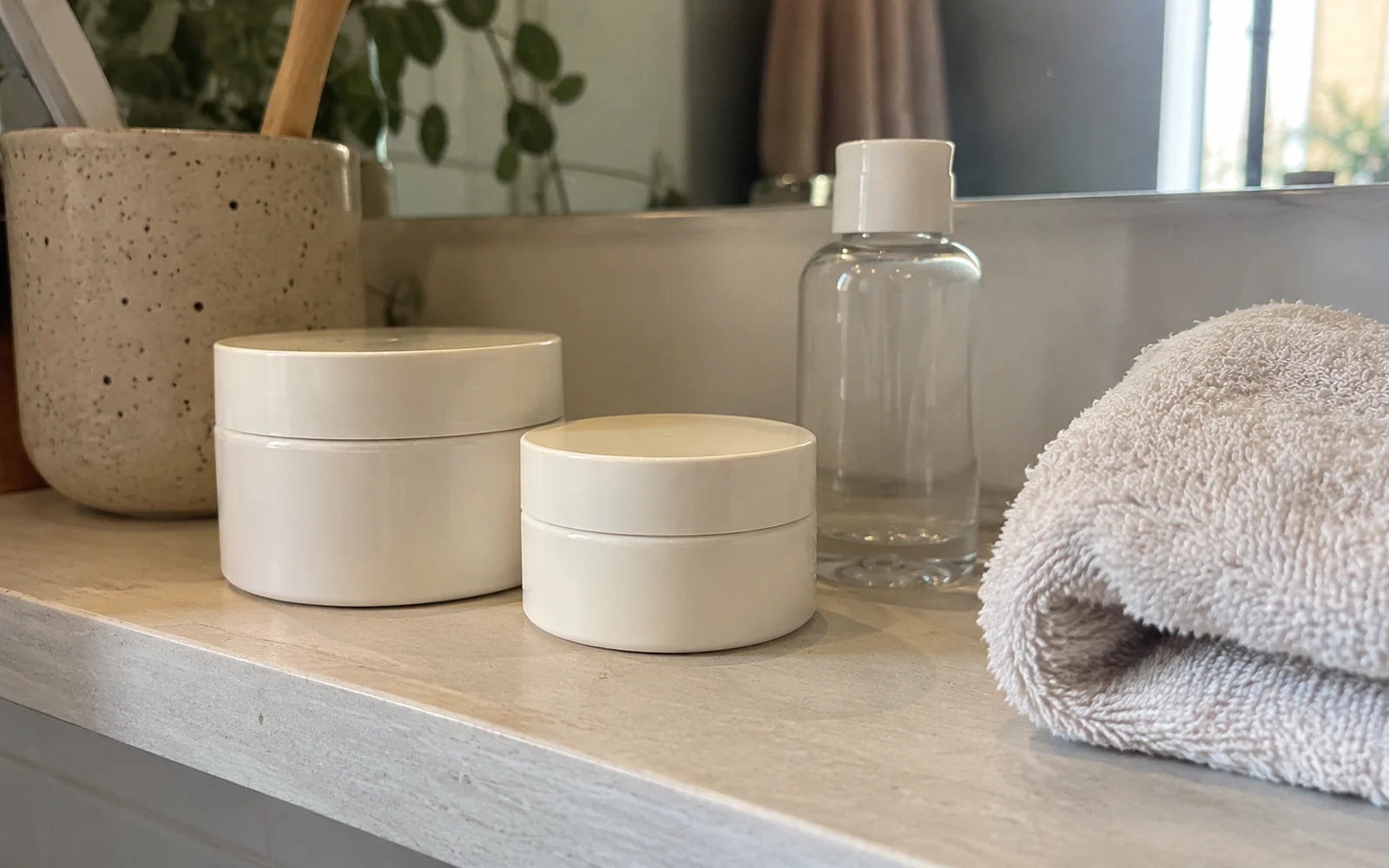 Deux pots cosmétiques fermés sans marque et un flacon transparent sur une étagère.