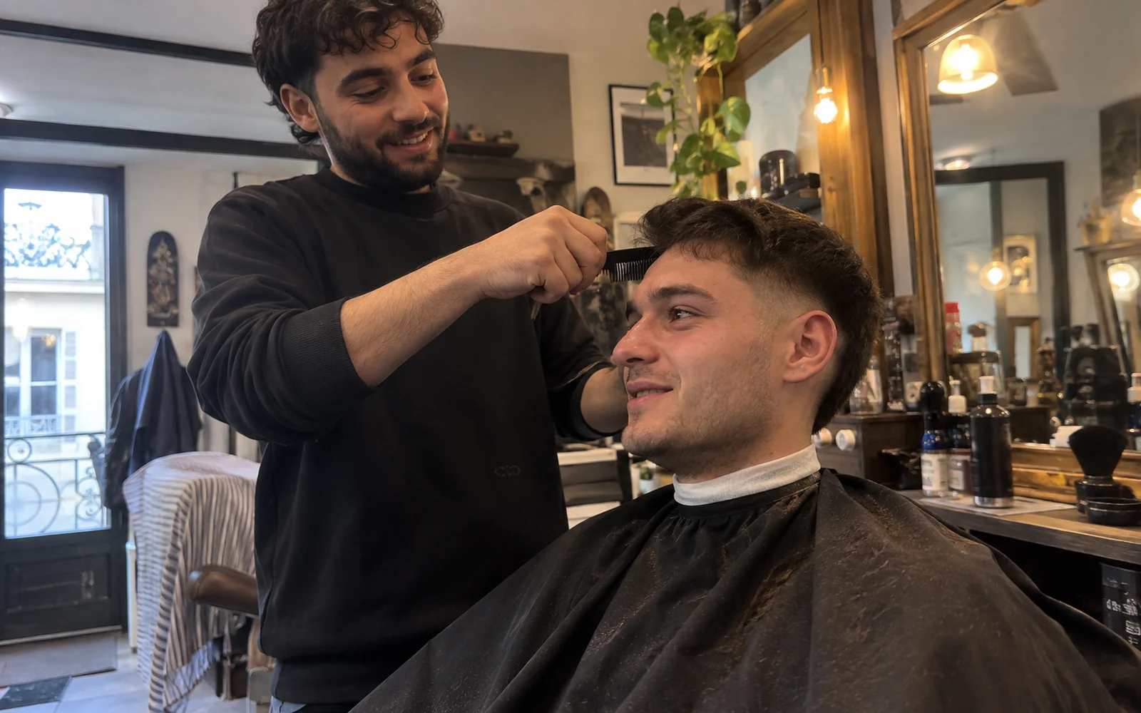 Jeune homme chez le barbier qui vérifie la ligne de ses cheveux avec un peigne.