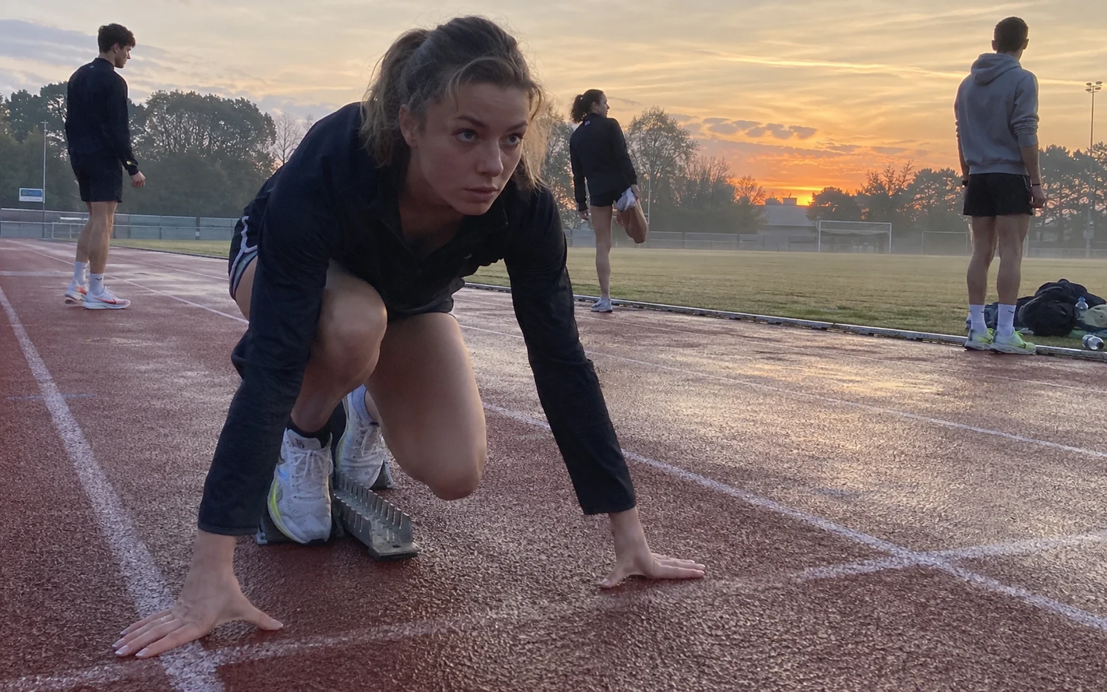 Sprinteuse en position de départ sur une piste d’athlétisme à l’aube.