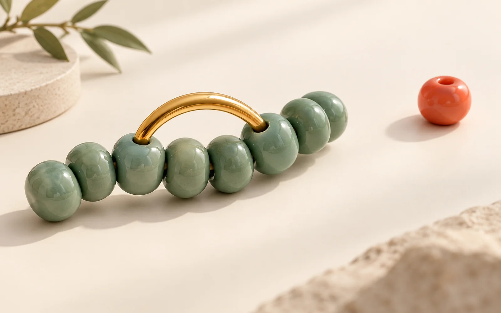 Vue d’artiste : une chaîne de perles jade reliée par un raccord ambré sur un fond crème.