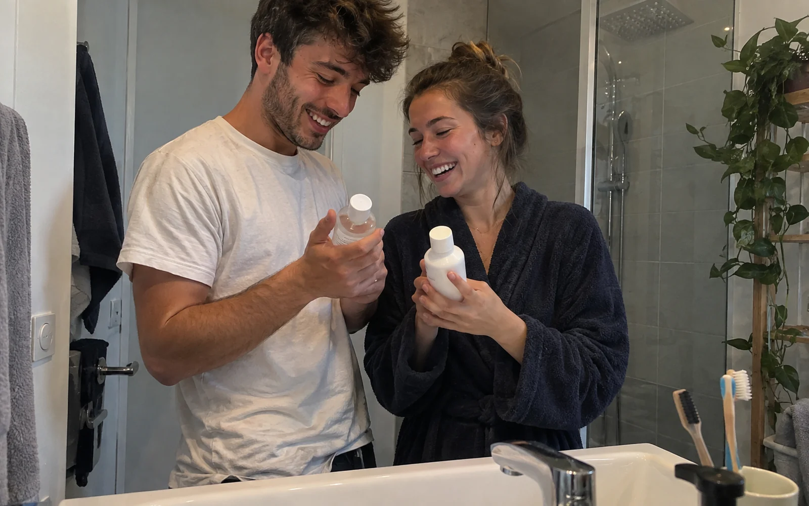 Jeune couple comparant deux flacons de soin sans étiquette devant le lavabo de la salle de bain.